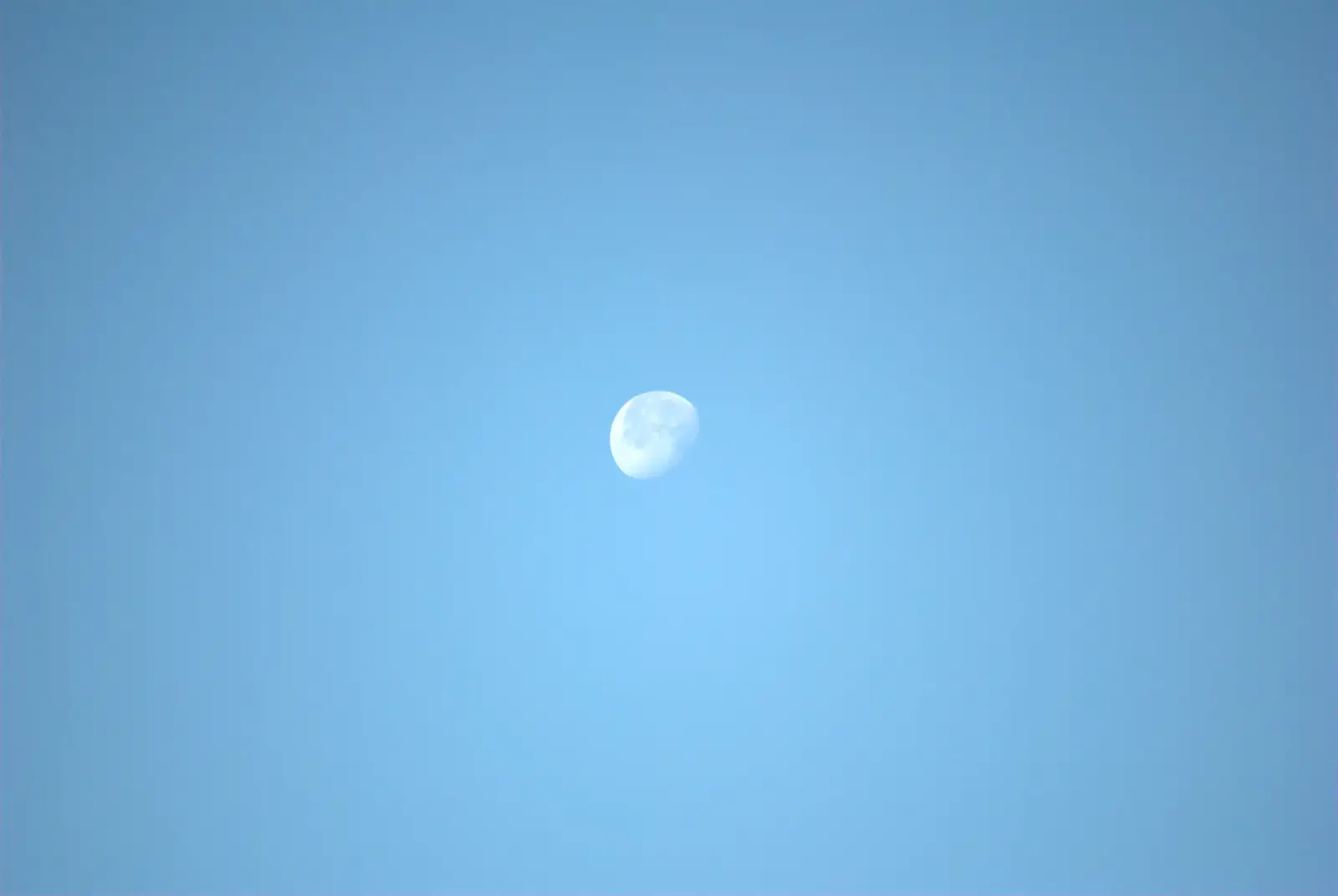 Pale moon suspended in a clear blue sky
