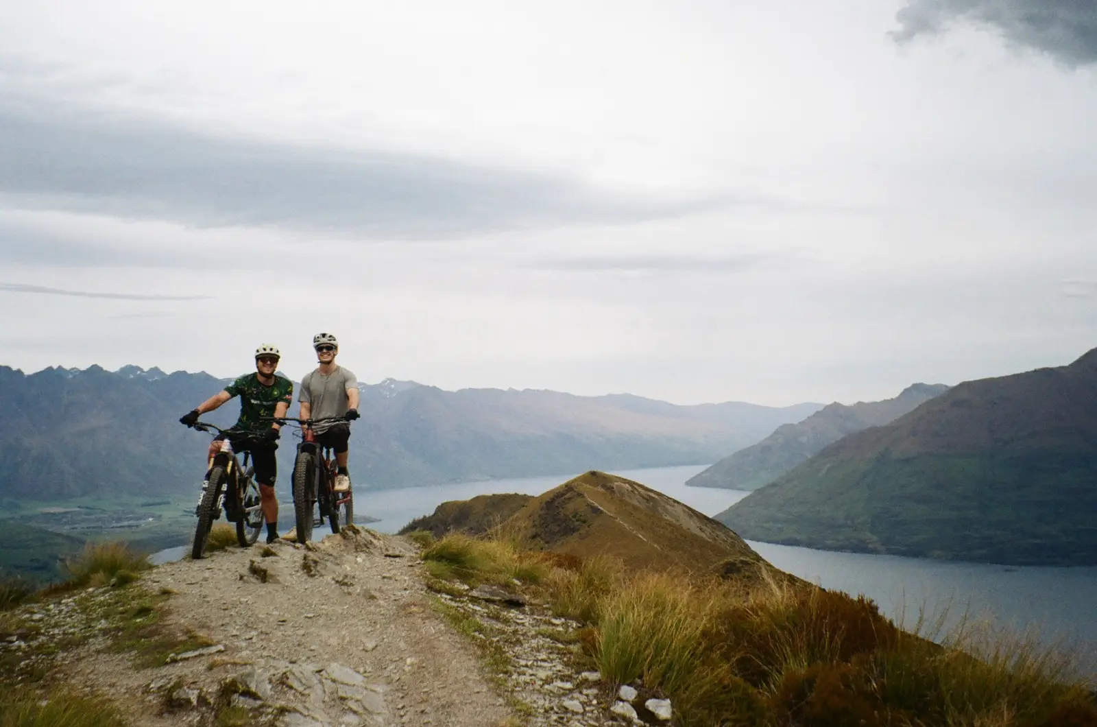 Two mountain bikers on a ridge above a long alpine lake