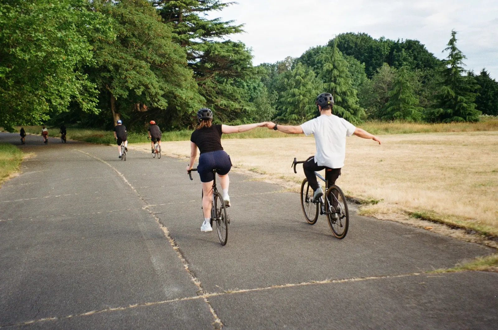 Two cyclists holding hands while riding through a park