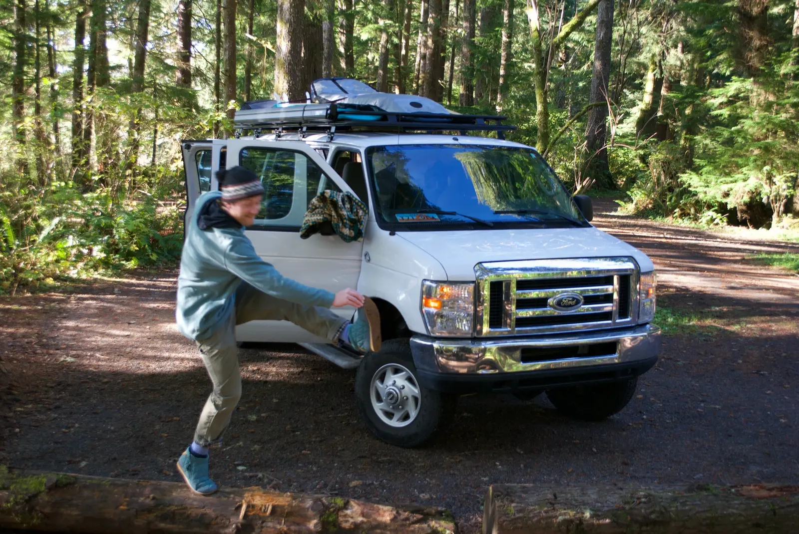 Person kicking playfully beside a white camper van in the forest