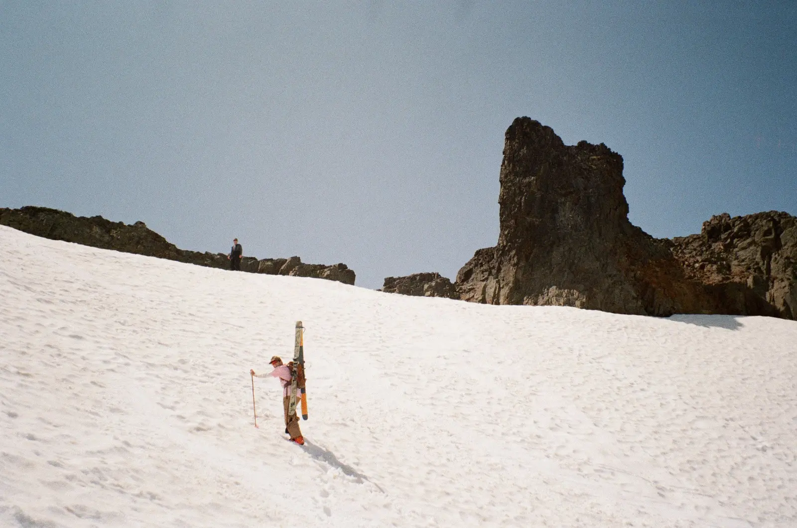 Skier climbing a broad snowfield beneath a rock formation
