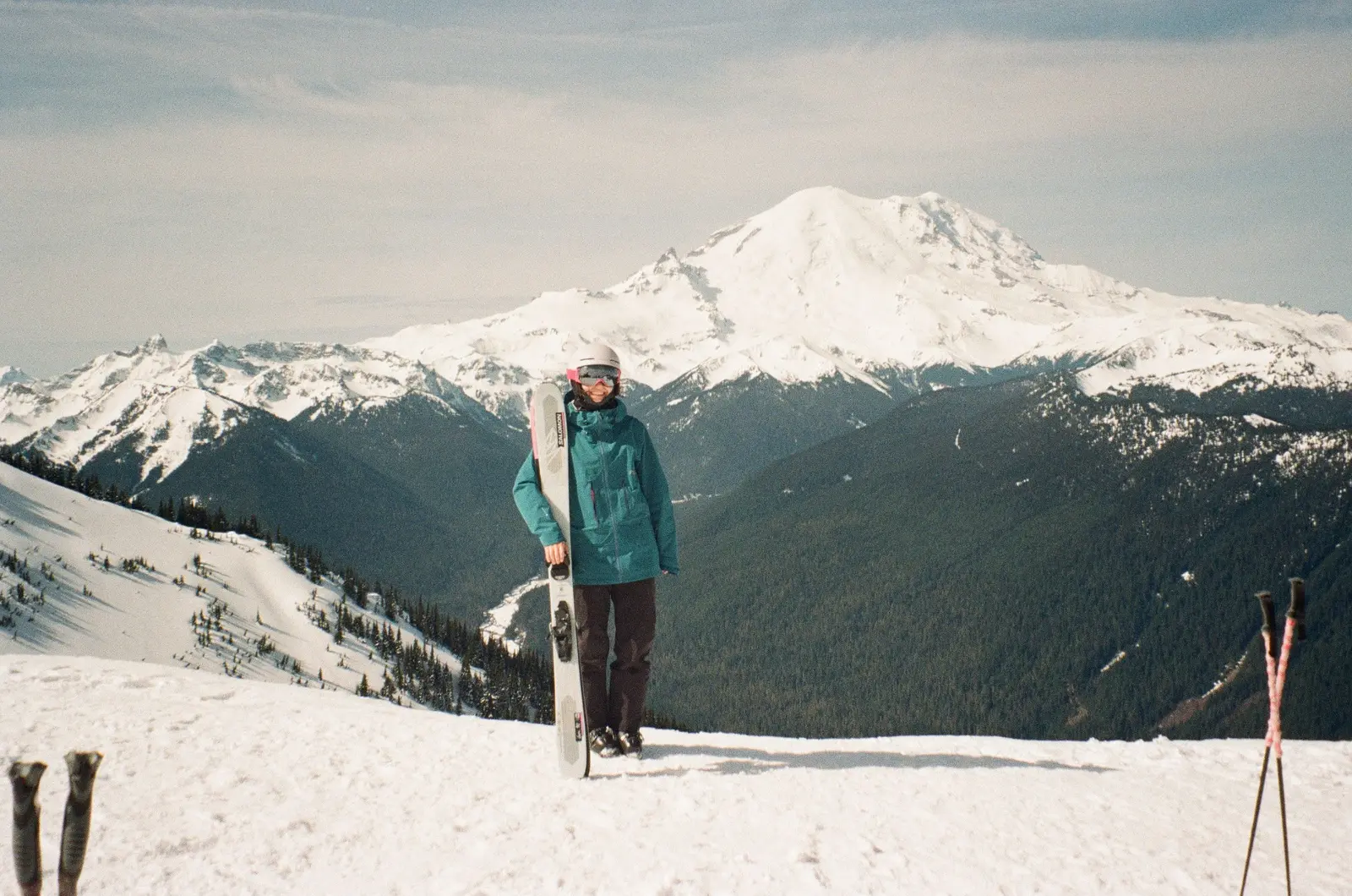 Skier in a teal jacket posing in front of a snowy mountain