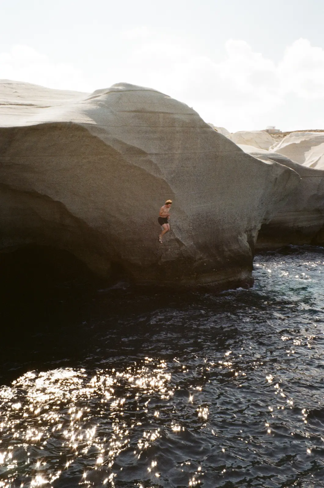 Person jumping from a dark rock ledge into sunlit water